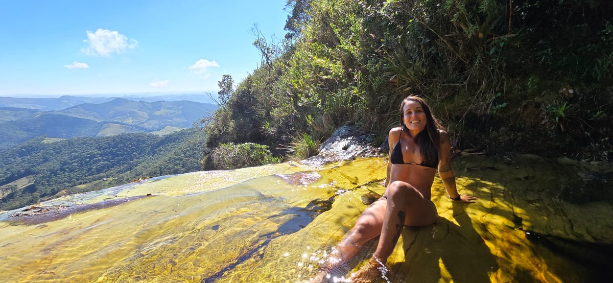 Thaíssa sentada numa laje de pedra, com os pés dentro de um rio de água dourada