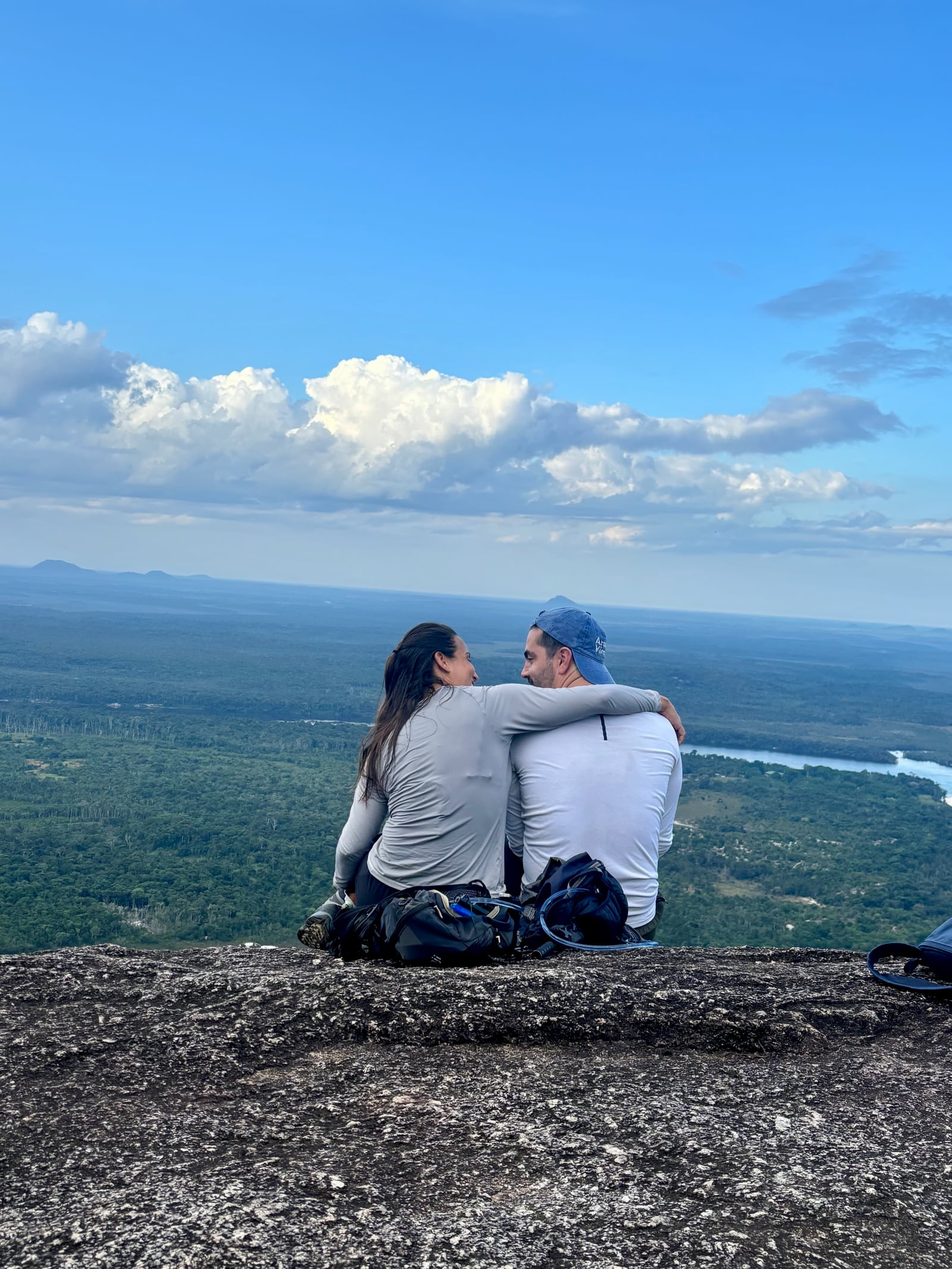 Thaíssa e Julián sentados de costas, olhando o vale aberto lá embaixo